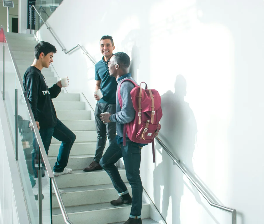 Three colleagues with coffee chatting on an office staircase