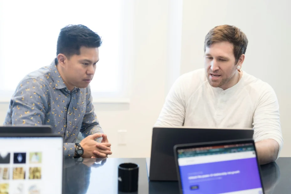 Two colleagues discussing work at laptops in a bright office